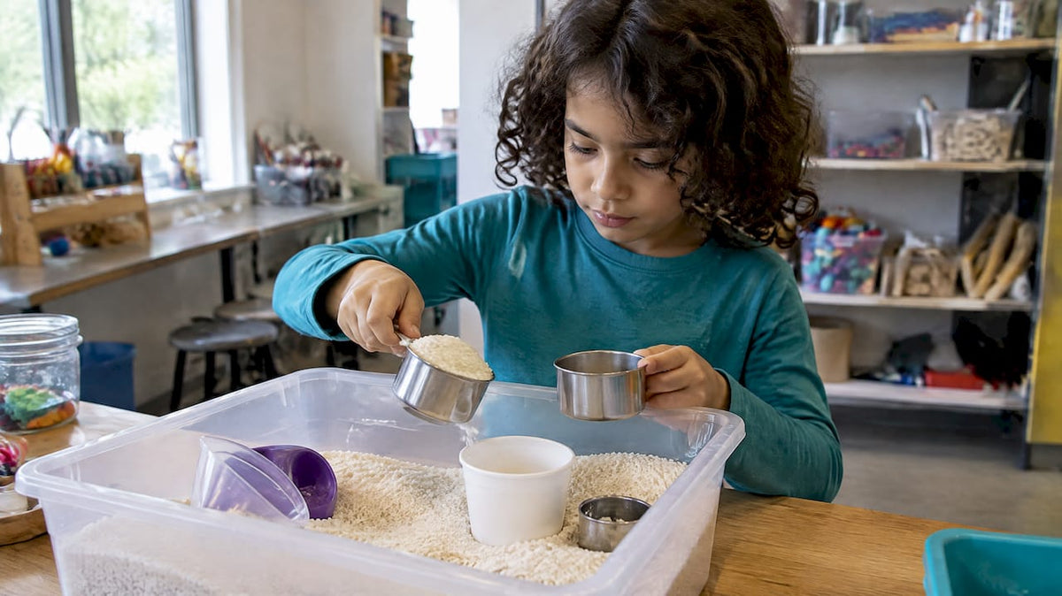 Child testing cups in a rice sensory bin